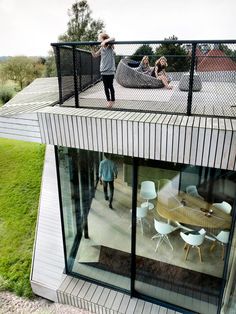 two people standing on the roof of a house with glass walls and sliding doors that open up to an outdoor deck area