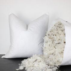 two white pillows sitting next to each other on top of a black table with a fur pillow