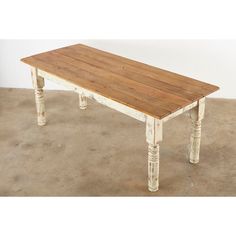 an old white table with wood top on concrete floored area in front of wall