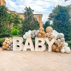 a sign that says baby in front of some trees and bushes with balloons on it