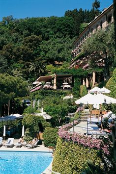 an outdoor swimming pool surrounded by trees and lawn chairs with umbrellas on the side