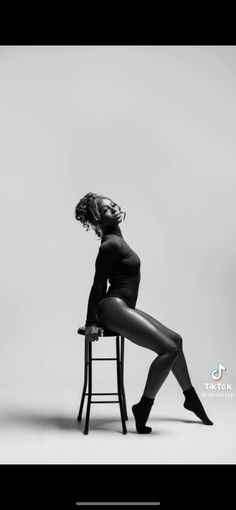 a woman sitting on top of a chair next to a white wall in black and white