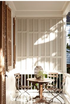 a table and chairs on a porch with shuttered walls in the backround