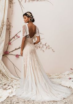 a woman in a wedding dress standing next to a wall with branches and flowers on it