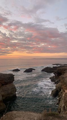 an ocean view with rocks in the foreground and pink clouds in the sky above