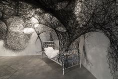 an artistic photo of a bed in a room with branches on the walls and ceiling