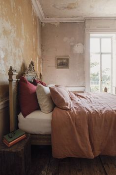 a bed sitting in a bedroom next to a window with lots of pillows on top of it