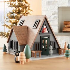 a wooden toy house sitting on top of a table next to a christmas tree and fire place