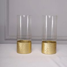 two gold colored glass vases sitting on top of a white tablecloth covered floor