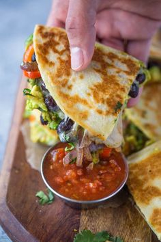 a person dipping salsa into a tortilla that is on a wooden platter