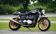 a black and gold motorcycle parked on the side of the road in front of some trees