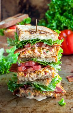 a bacon, lettuce and tomato sandwich on a cutting board with tomatoes in the background