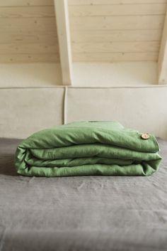 a green blanket is folded on top of a gray bed with white sheets and pillows