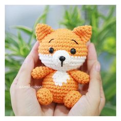 a small crocheted orange and white teddy bear sitting in front of some plants