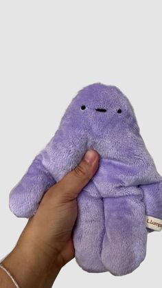 a hand is holding a purple stuffed animal