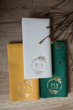 three different colored napkins sitting next to each other on a wooden table with dried flowers