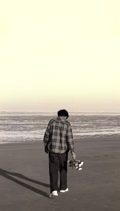 a man standing on top of a beach next to the ocean holding a skateboard