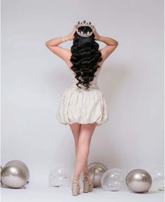 a woman wearing a tiara standing in front of silver balls and balloons with her back to the camera