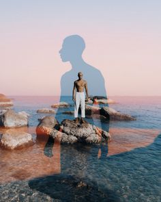 a man standing on top of a rock in the ocean next to a body of water