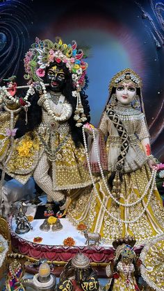 two dolls dressed in gold and white are standing next to each other on a table