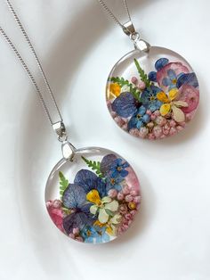 two necklaces with flowers in them on a white surface