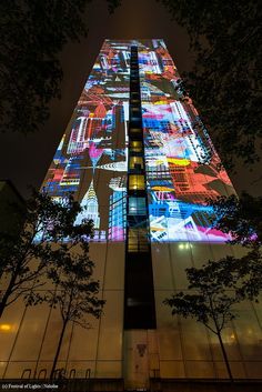 a tall building with colorful lights on it's side and trees in the foreground