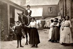 an old black and white photo of people standing around with a child on a horse