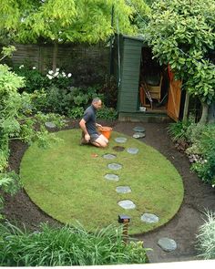 a man kneeling down in the middle of a garden with stepping stones on the ground