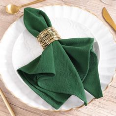 a green napkin on a white plate with gold fork and spoons next to it