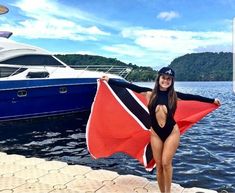 a beautiful woman in a bathing suit standing next to a boat with a flag on it