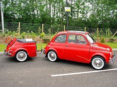 an old red car parked in a parking lot next to another classic car with the door open