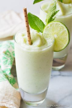 two glasses filled with lemonade and mint on top of a white tablecloth next to other glassware