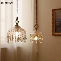 two glass chandeliers hanging from a ceiling in a room with white walls and curtains