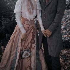 a man and woman dressed in victorian clothing posing for a photo together, with leaves on the ground around them