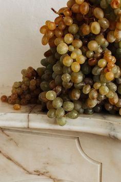 a bunch of grapes sitting on top of a white marble shelf next to a wall