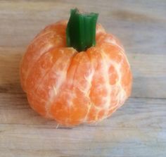 an orange sitting on top of a wooden table next to a green piece of fruit