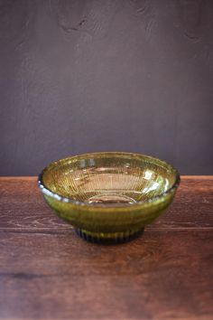 a green glass bowl sitting on top of a wooden table next to a brown wall