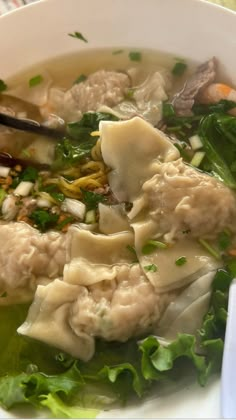 a white bowl filled with dumplings and greens