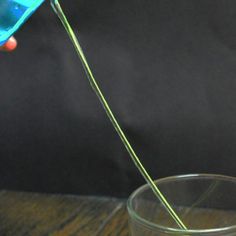 a person is pouring something into a glass with a blue substance in it on a wooden table