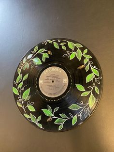 a black record with green leaves painted on the front and sides, sitting on a table