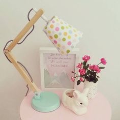 a pink table topped with a potted plant next to a lamp and photo frame