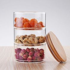 three glass containers filled with dried fruits and flowers on top of a wooden table next to a jar