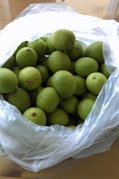 a plastic bag filled with green apples on top of a wooden table