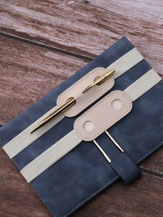 a small blue and white notebook with two gold pins on the front, sitting on a wooden surface