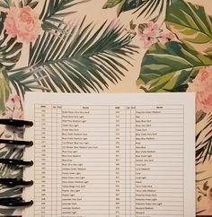 an open planner with pink flowers and palm leaves on the cover, next to a black pen