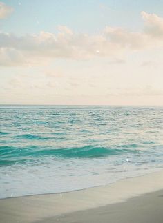 a woman walking along the beach with her surfboard in hand and water behind her