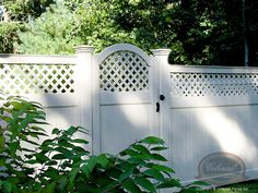 a white fence with an arched top and lattice design on the gate is surrounded by greenery