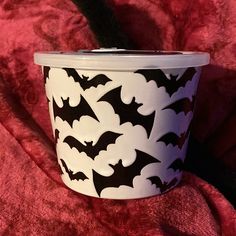 a white cup with black bats on it sitting on a red blanket next to a cat