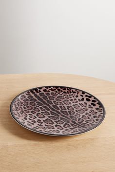 a brown and black plate sitting on top of a wooden table next to a white wall