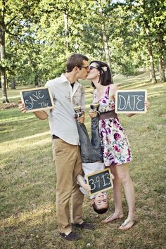 a man and woman kissing while holding chalkboards that say save the date in front of them